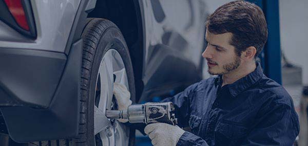 Auto mechanic uses air drill on car wheel