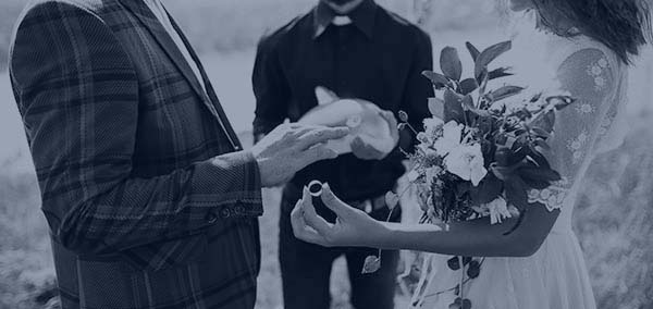 Monotone blue tinted image of bride, groom, and wedding officiant